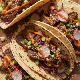 Korean BBQ Tacos with bulgogi beef, cabbage, pickled radish, and gochujang sauce on charred tortillas