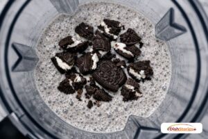 Broken Oreo cookie pieces being added to a blended milkshake to ensure a crunchy texture.