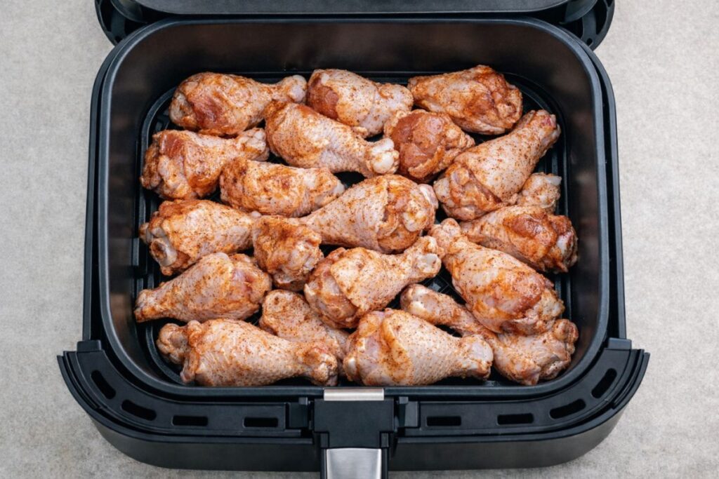Top‑down view of raw, seasoned chicken pieces arranged in the Cosori TurboBlaze 6‑quart air fryer basket before cooking, showing the square black design and perforated tray on a light countertop.